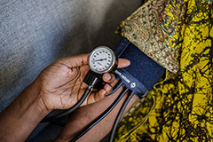A closely-cropped image showing a blood pressure cuff on one person's arm and another hand reading the meter in the foreground.
