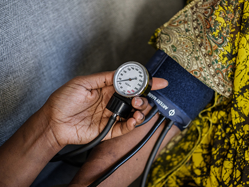 A closely-cropped image showing a blood pressure cuff on one person's arm and another hand reading the meter in the foreground.