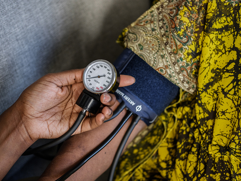 A closely-cropped image showing a blood pressure cuff on one person's arm and another hand reading the meter in the foreground.