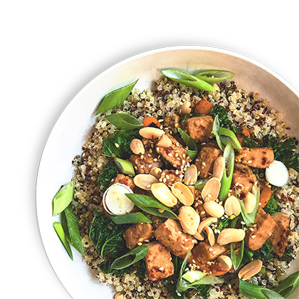 A bowl of tricolor quinoa topped with Quorn Vegan PIeces in a sticky orange sauce, tenderstem broccoli, green onions, peanuts, and sesame seeds.