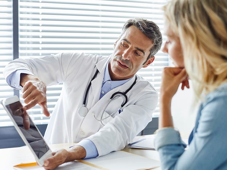 A male doctor showing a tablet to a woman in a blue top.